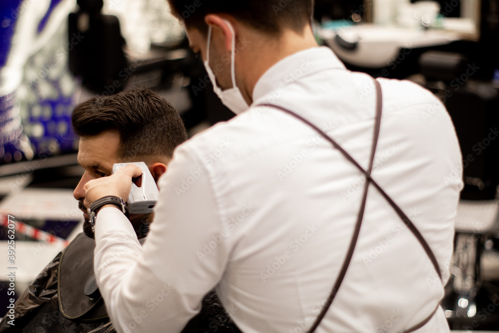 Young barber on his back wears a mask while working
