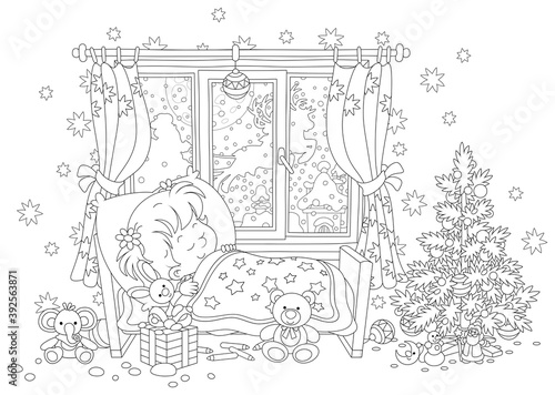 Cute little girl sleeping in her small bed on the night before Christmas, in a window of a nursery room magic reindeers flying Santa Claus with holiday gifts in his sleigh over snowy town