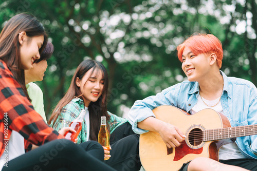 group of happy Asian young people sitting on the guitar and singing in the park
