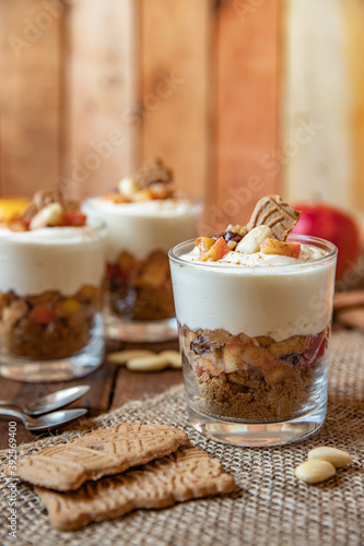 Kuchen im Glas mit Stücken vom Bratapfel, Zimt, Spekulatius, Apfel, Mandeln und Rosinen mit einer Creme aus Quark oder Mascarpone auf einem Tisch aus Holz in einer gemütlichen Küche zu Weihnachten