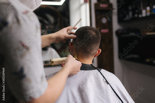 Professional hairdresser uses a hair clipper for fringing hair for a handsome bearder man. Barbershop
