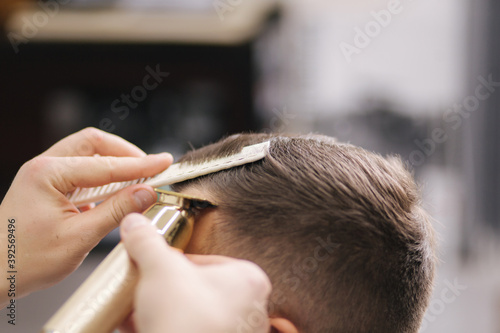 Professional hairdresser uses a hair clipper for fringing hair for a handsome bearder man. Barbershop