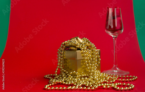 ..Wine glass and gold gift box with beads on a red-green background. The concept of a gift for a girl for a holiday. Close-up Selective focus.