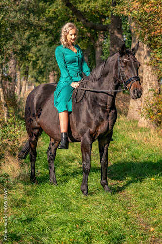 Young blonde girl in a vintage green dress with a big skirt posing with a brown horse. Selective focus