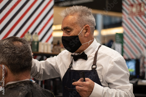 Elderly barber cuts an old man's hair while holding a comb © Alberto Cotilla