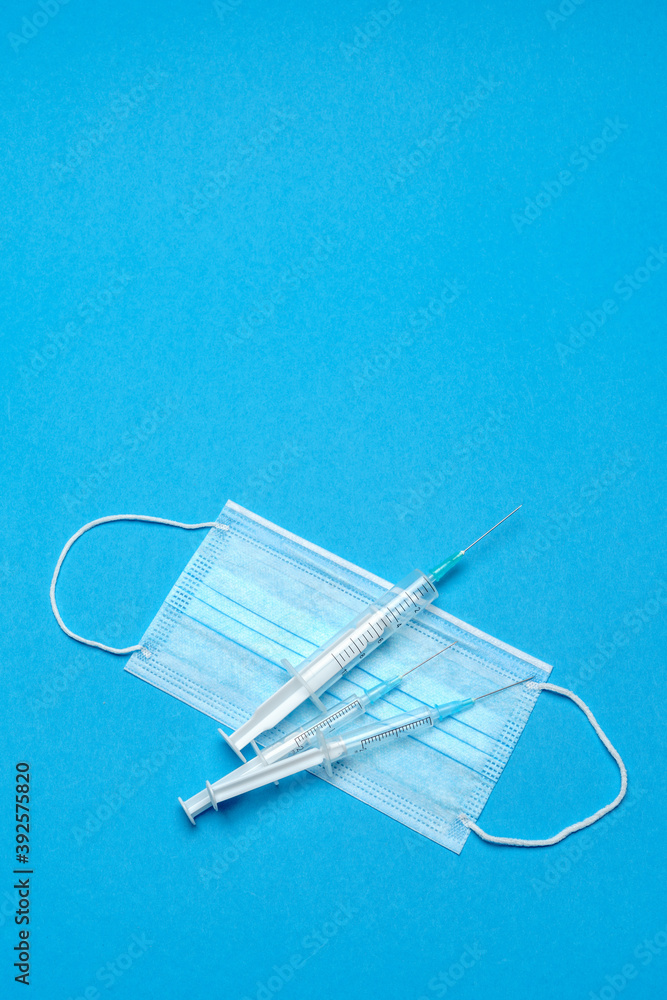 Syringe and disposable face mask to prevent COVID-19 virus on blue background Syringe and disposable face mask to prevent COVID-19 virus on blue background