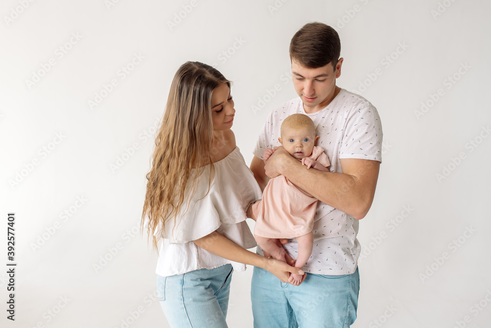Young caucasian beautiful parents mom and dad hug and kiss their newborn daughter while standing on a white background
