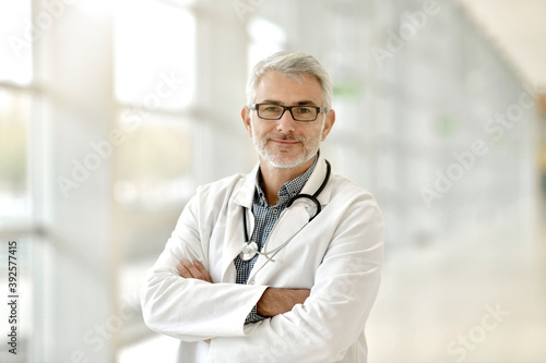 Portrait of confident doctor with grey hair standing in hospital hallway photo