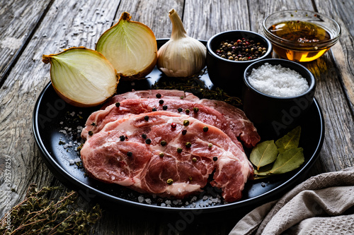 Raw pork chops with onion garlic and seasonings on plate on wooden table