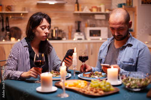 Couple dining together using smartphone in kitchen. Adults sitting at the table  browsing  searching  using smartphones  internet  celebrating anniversary.