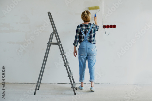 Young woman makes repairs in her house, next to a stepladder, holds a tool in her hands