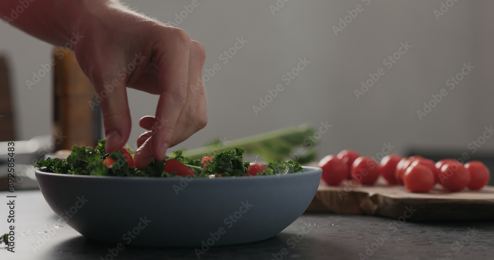 Slow motion man hands put tomatoes on top of kale in blue bowl on concrete surface