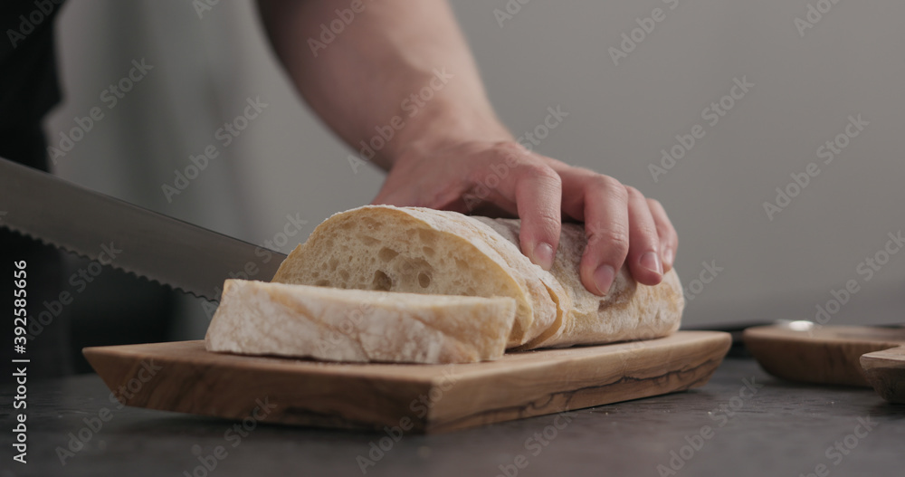 Slow motion man slicing ciabatta with bread knife on olive board Slow motion man slicing ciabatta with bread knife on olive board