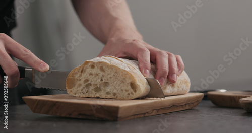 Slow motion man slicing ciabatta with bread knife on olive board