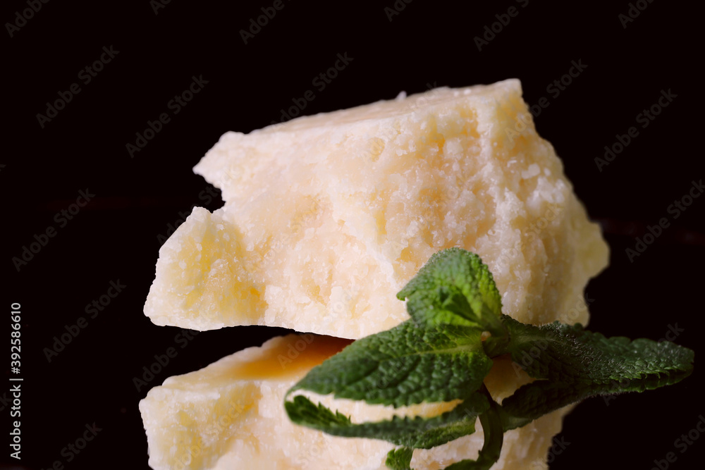 Piece of hard cheese on a black background. Reflection of a piece of cheese in a mirror surface. Close-up, side view. Piece of hard cheese on a black background. Reflection of a piece of cheese in a mirror surface. Close-up, side view.