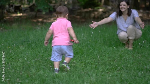 Young mother plays with her son in nature. Baby's first steps. Public park. Camera fly