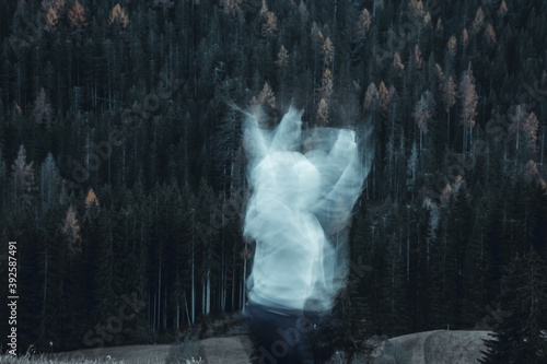 Long exposure shot of subject in movement, creating a ghost or spirit or ectoplasm appearing just outside a thick forest. photo