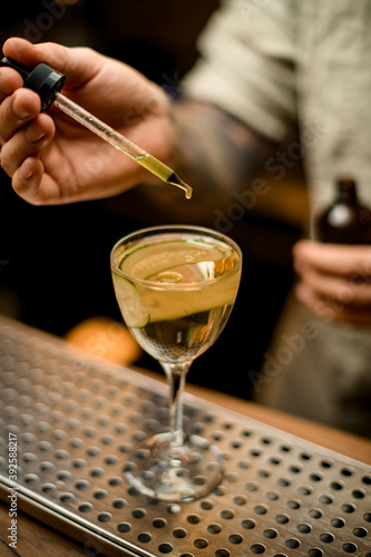 bartender holds dropper with liquid and adds it to wine glass with cocktail © fesenko