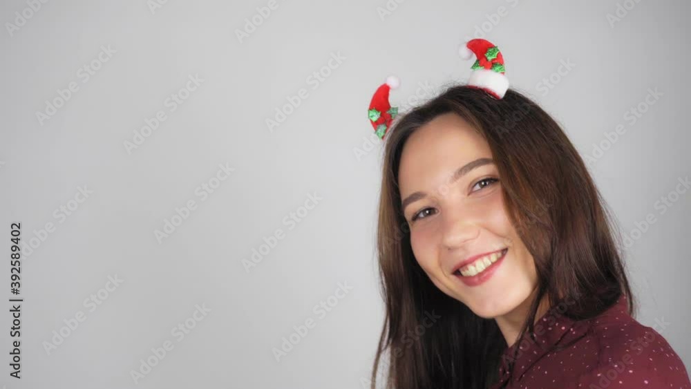 Happy brunette woman with Christmas decoration in her hair sends an air kiss. Light background.
