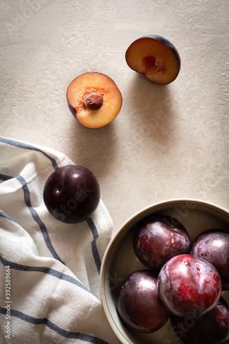 A bowl of ripe plums on a striped napkin and scattered plums on a marble top. Flatlay photo.