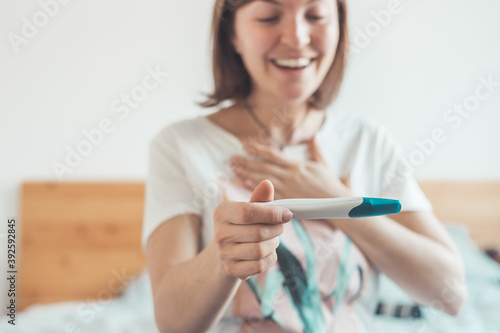 Happy woman sitting on the bed, checking pregnancy test. Result positive, “Schwanger”
