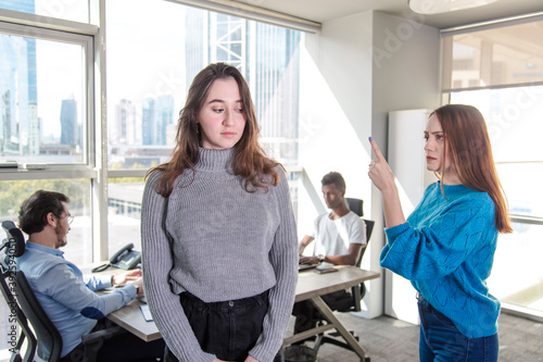 a brunette unhappy woman is exposed to discrimination and harrassment in a modern office from the woman director n front of their colleagues.