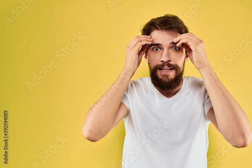 A man in a white t-shirt gestures with his hands lifestyle cropped view yellow background more fun © SHOTPRIME STUDIO