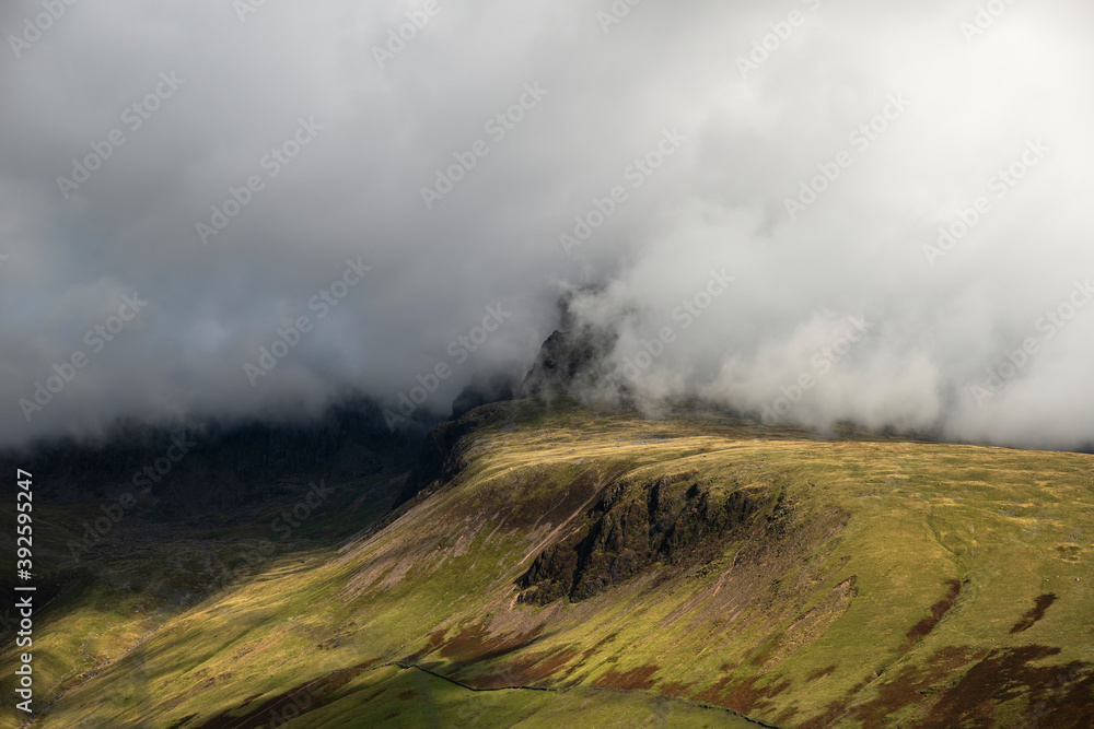 Stunning landscape image of low cloud on the peak of England's highest mountain, Scafell Pike with stunning light on the mountainside