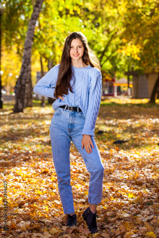 Young brunette girl in a woolen sweater and blue jeans posing in an autumn park Young brunette girl in a woolen sweater and blue jeans posing in an autumn park