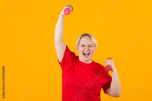 beautiful young plump female in a red t-shirt with dumbbells on a yellow background © Alexandr