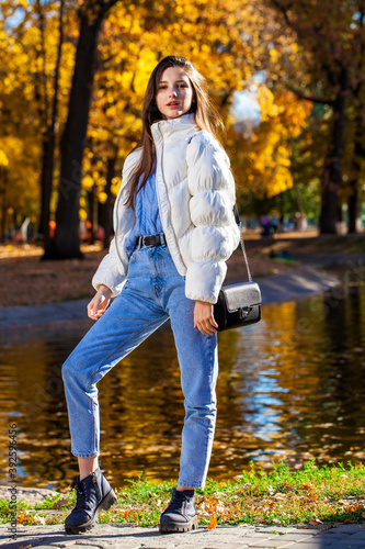 Young brunette girl in a woolen sweater and blue jeans posing in an autumn park