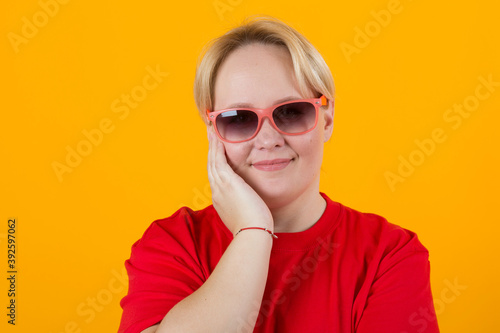 beautiful young plump female in a red t-shirt on a yellow background with glasses