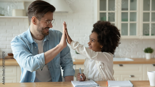 Smiling father and African American little girl giving high five  celebrating success  adorable girl with happy dad studying together  teacher supporting pupil  multiracial family  homeschooling