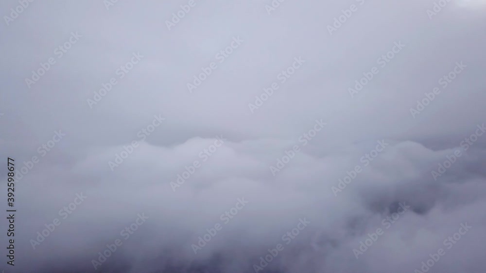 Flying among several layers of clouds over the city. Large Cumulus clouds are dark gray with a hint of blue. Winter landscape of sky above Almaty. View from a drone. The sun's disk is visible in fog. Flying among several layers of clouds over the city. Large Cumulus clouds are dark gray with a hint of blue. Winter landscape of sky above Almaty. View from a drone. The sun's disk is visible in fog.