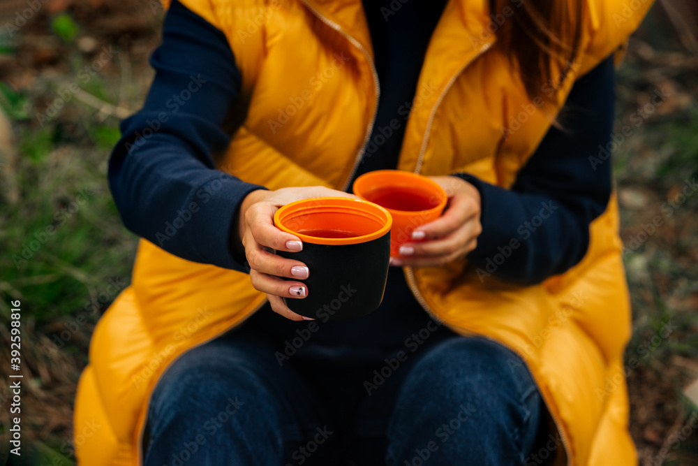 Drinking tea during hike. Woman giving a cup of hot tea from black thermos bottle. Refreshment during hiking Drinking tea during hike. Woman giving a cup of hot tea from black thermos bottle. Refreshment during hiking