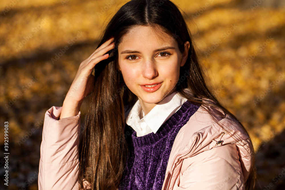 Close up portrait of a young beautiful woman in beige coat in autumn park