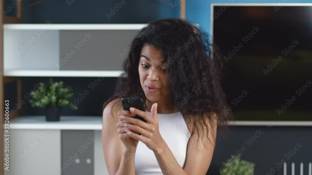 Shocked African American young woman looking at smartphone and shows disgust. Unpleasantly surprised girl with bad news. Shocked African American young woman looking at smartphone and shows disgust. Unpleasantly surprised girl with bad news.