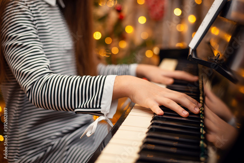 Close-up shot of girl`s hands on keyboard of a piano with christmas lights on the background. Christmas and New Year holidays photo