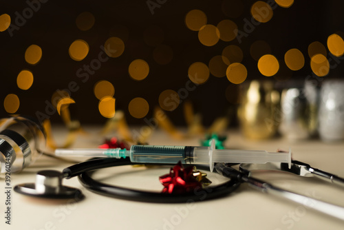 Jeringuilla vacuna covid-19 y estetoscopio sobre mesa de color cálido, coronavirus, regalo de navidad con lazo rojo y dorado,