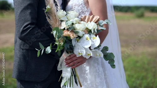 Young beautiful newlyweds couple holding wedding bouquet looking forward. True feelings. Bride kisses groom talking looking romantic eyes on flowers. Marriage proposal. Wedding day. Dating agency.