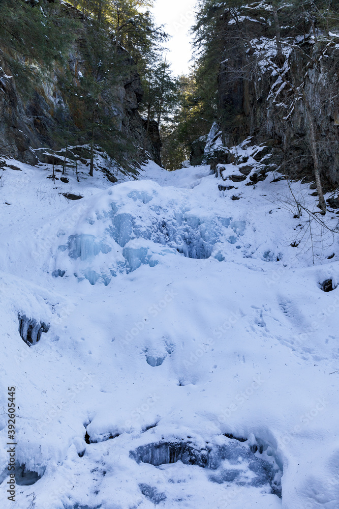 Moss Glen Falls in winter after snow storm. Water turned into ice and is covered with a snow. Bright sunny day.