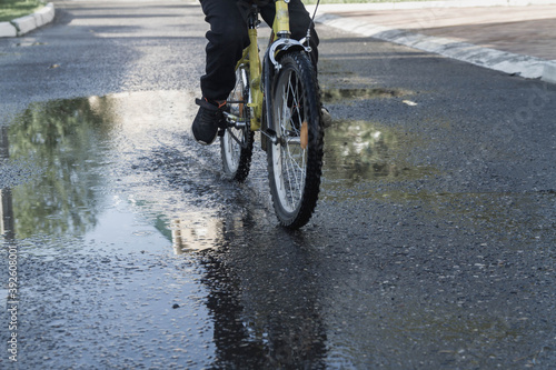 Fototapeta Naklejka Na Ścianę i Meble -  A man rides a Bicycle on the road. Puddles on the asphalt after the rain. Splashes and drops of water fly from under the wheel. The child quickly rolls through large puddles.