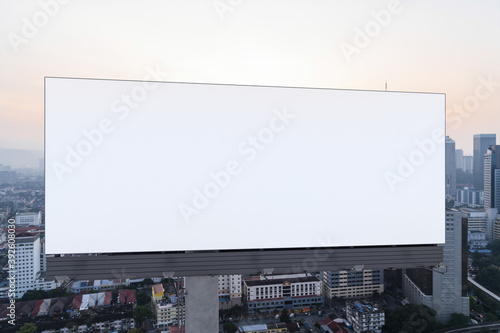 Blank white road billboard with Kuala Lumpur cityscape background at sunset. Street advertising poster, mock up, 3D rendering. Front view.