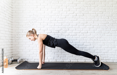 Young fit woman in black sportswear doing push ups at home