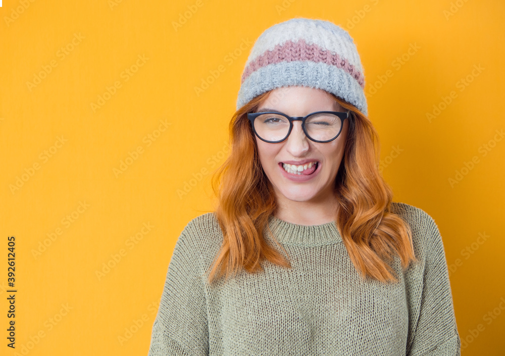 Happy woman blinks one eye, isolated on yellow background. Studio shot of cheerfully blond young girl