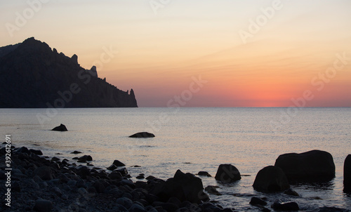 Early morning before sunrise on the Crimean coast. Beautiful view of the silhouette of Karadag mountain and pink dawn over the sea