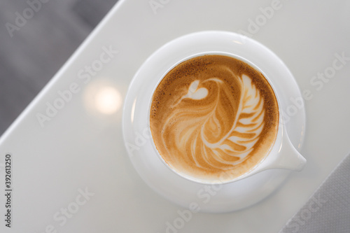 Top view of hot coffee with latte art in a white cup and saucer on white table background in the cafe.