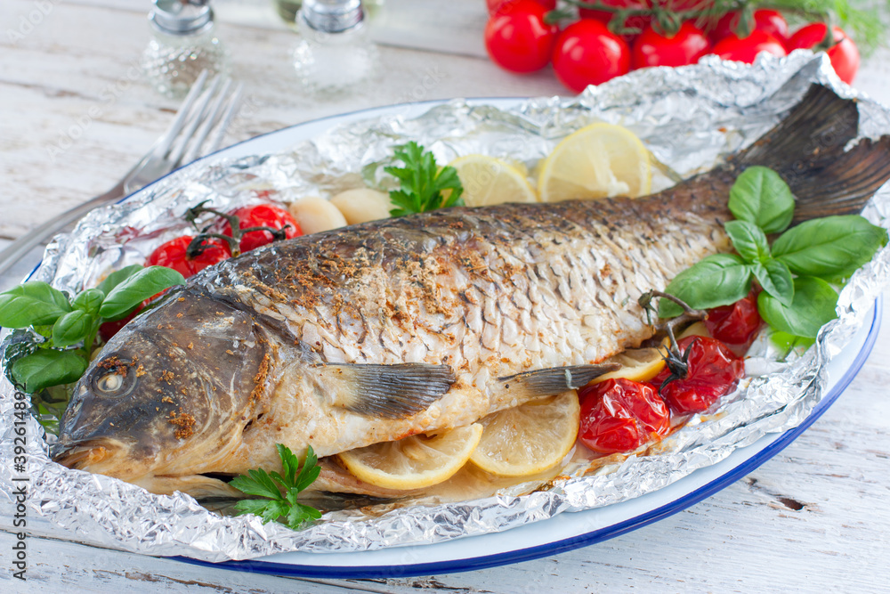 whole baked carp in foil with lemon in the oven on a wooden table, horizontal whole baked carp in foil with lemon in the oven on a wooden table, horizontal