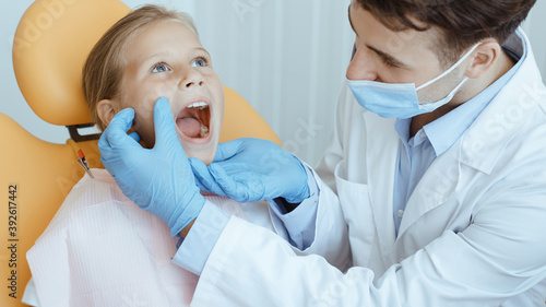 Hands of unrecognizable pediatric dentist making examination procedure for smiling cute little girl