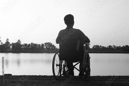 Silhouette young disabled man seeing river background.He is raise a hand to and sitting on wheelchair.despair,lonely,hope.Photo concept depression and Patient.